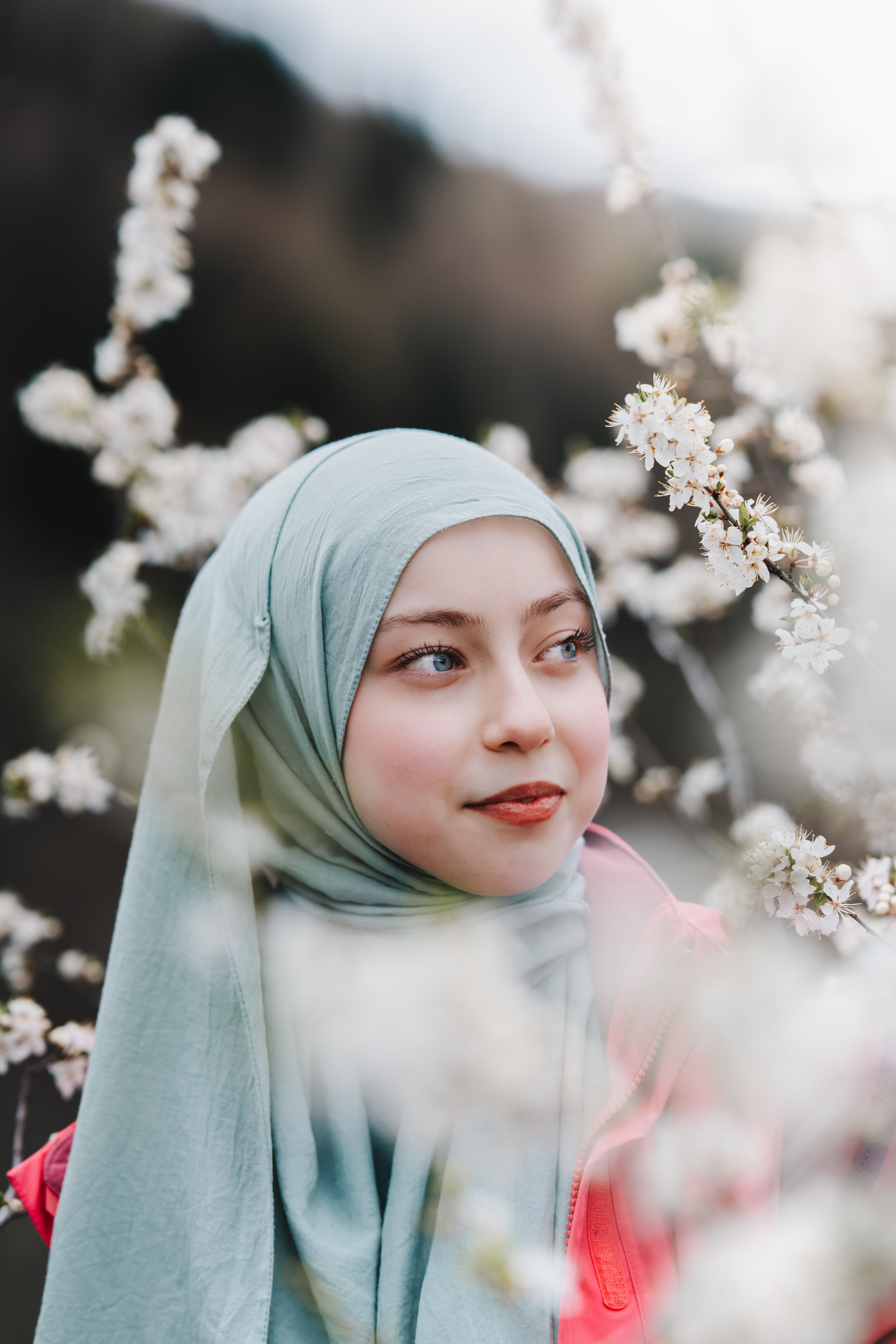 Serene portrait of a young woman wearing a headscarf surrounded by blooming cherry blossoms.