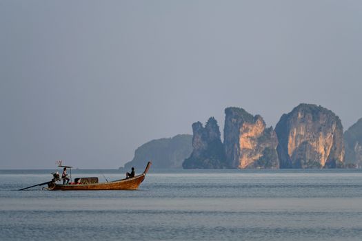 A peaceful longtail boat in the waters of Krabi, Thailand with dramatic cliffs in the background at dawn.