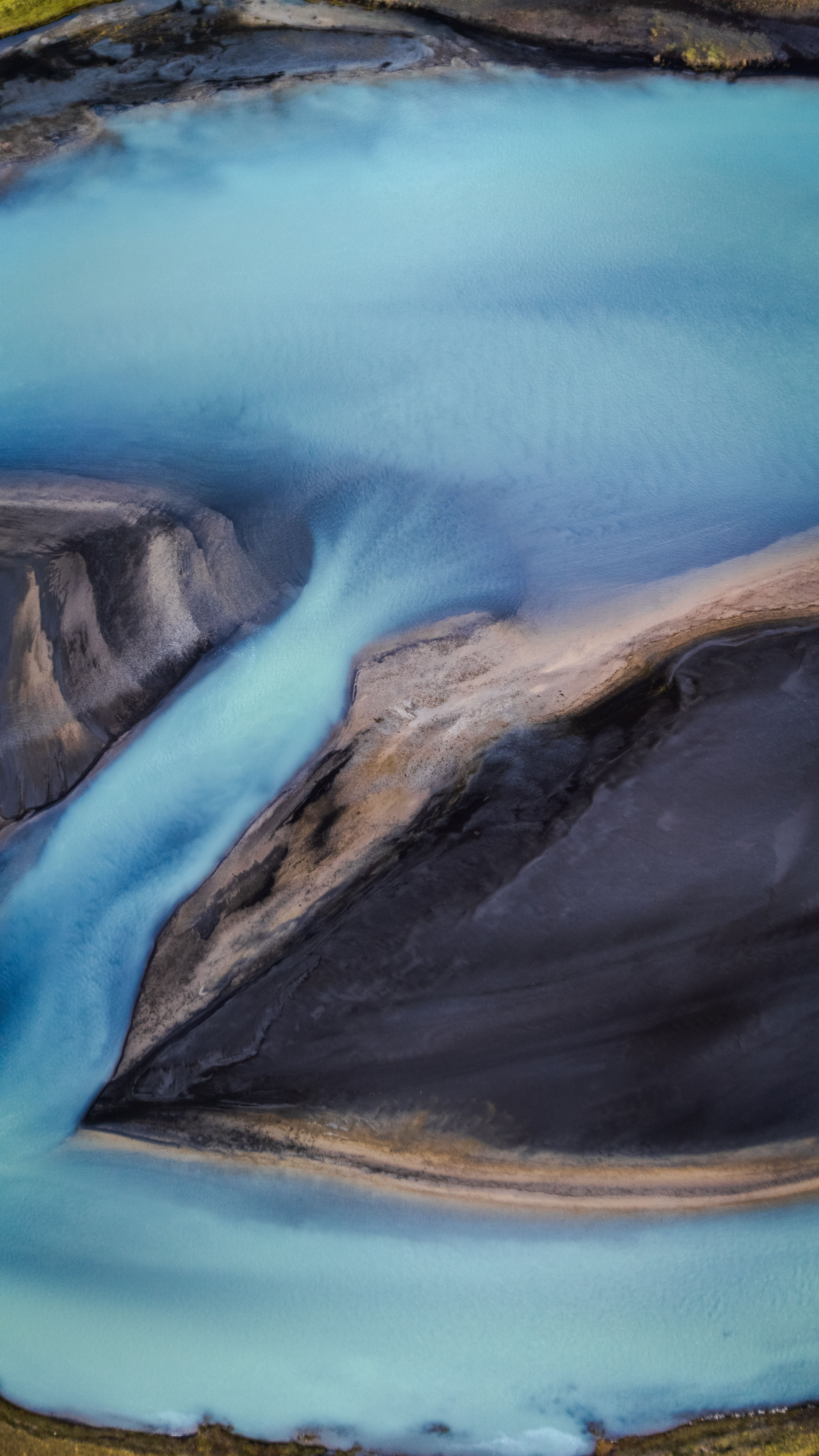 Aerial view of a winding blue river surrounded by dark rocky terrain on an island, offering a serene natural scene.