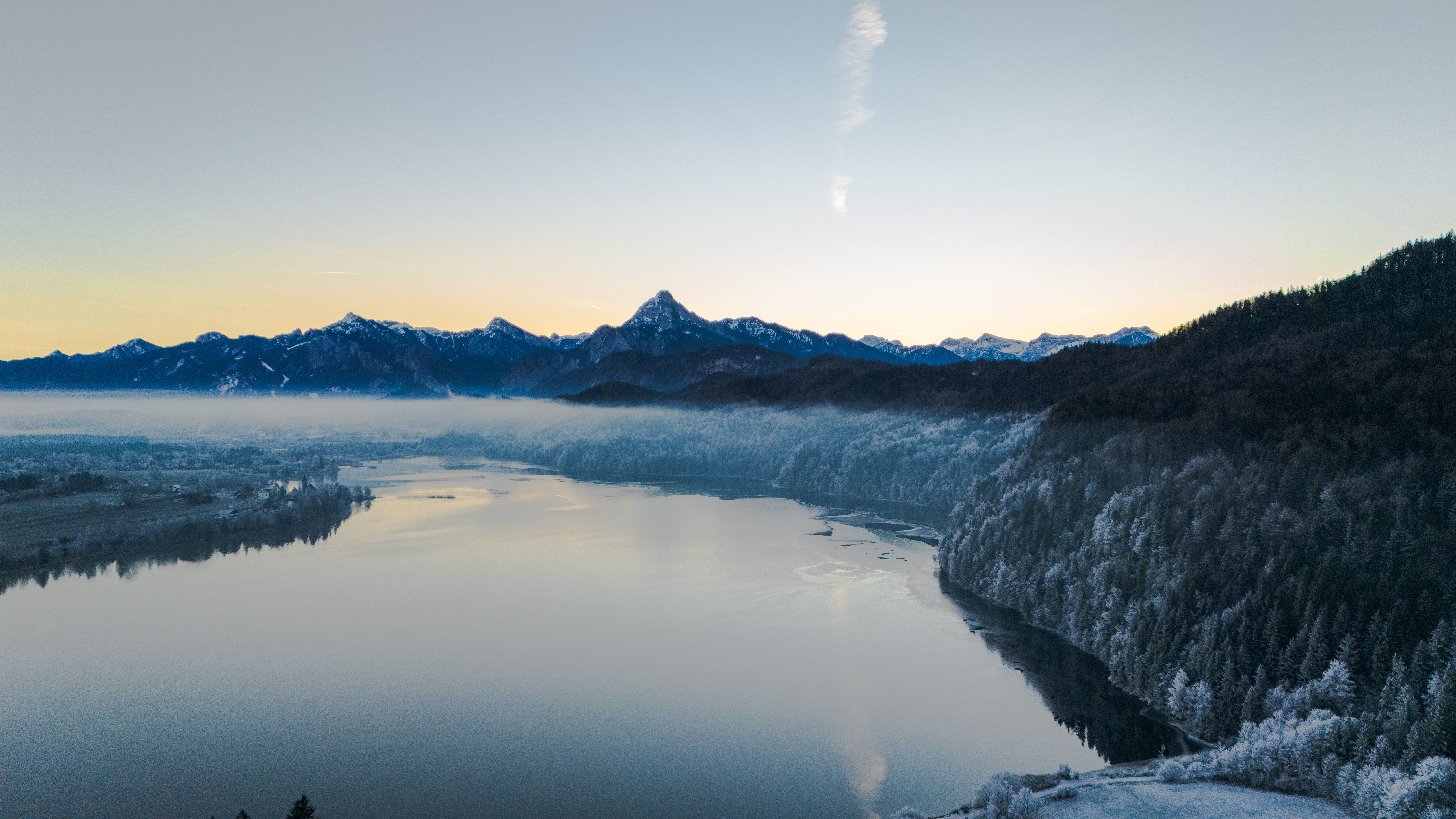 A breathtaking aerial view of a serene winter landscape at sunrise, showcasing icy mountains and a peaceful lake.