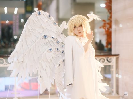Cosplay of an angelic figure indoors, featuring ornate wings adorned with eye designs.