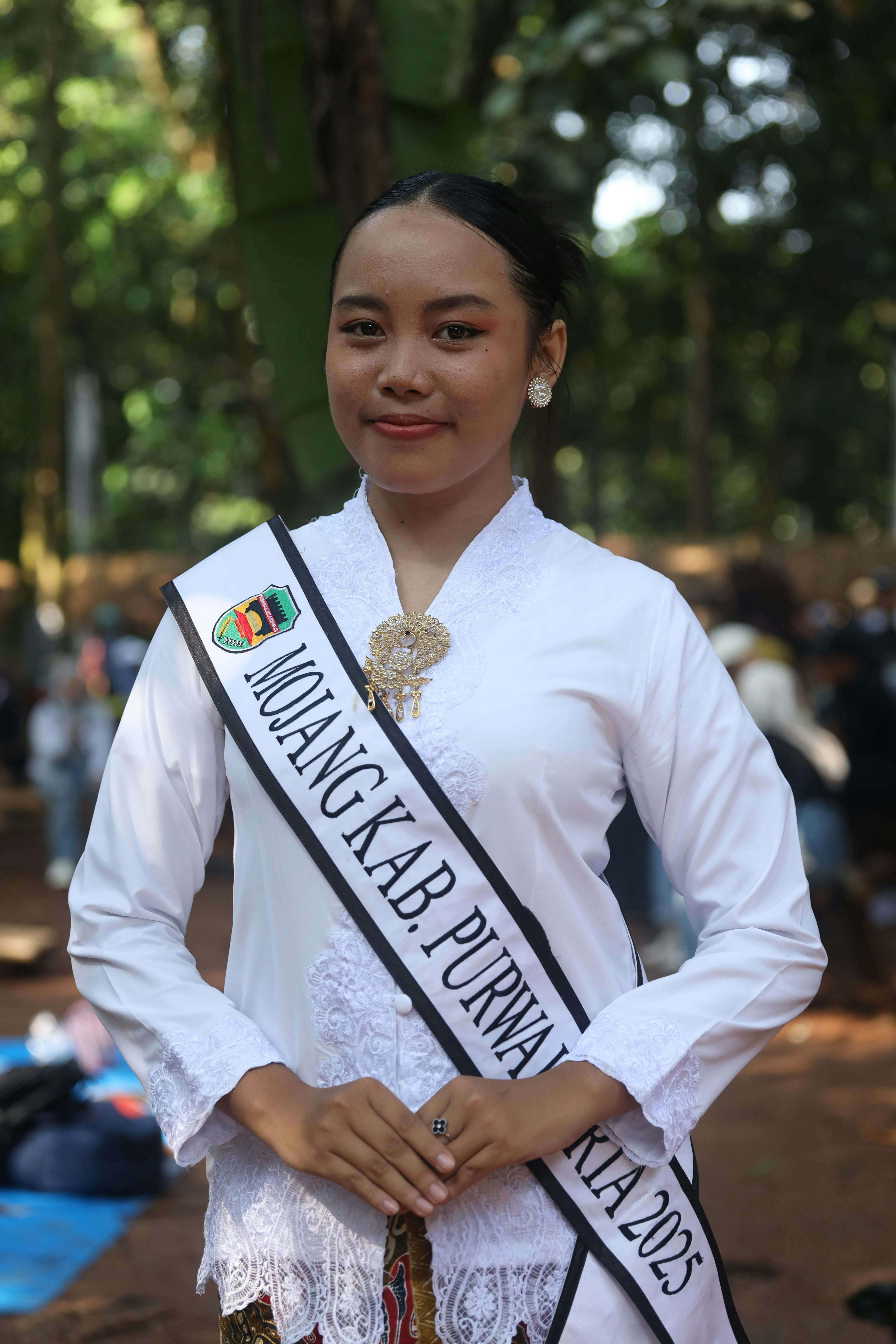 Young woman in traditional Indonesian attire at a pageant event outdoors.