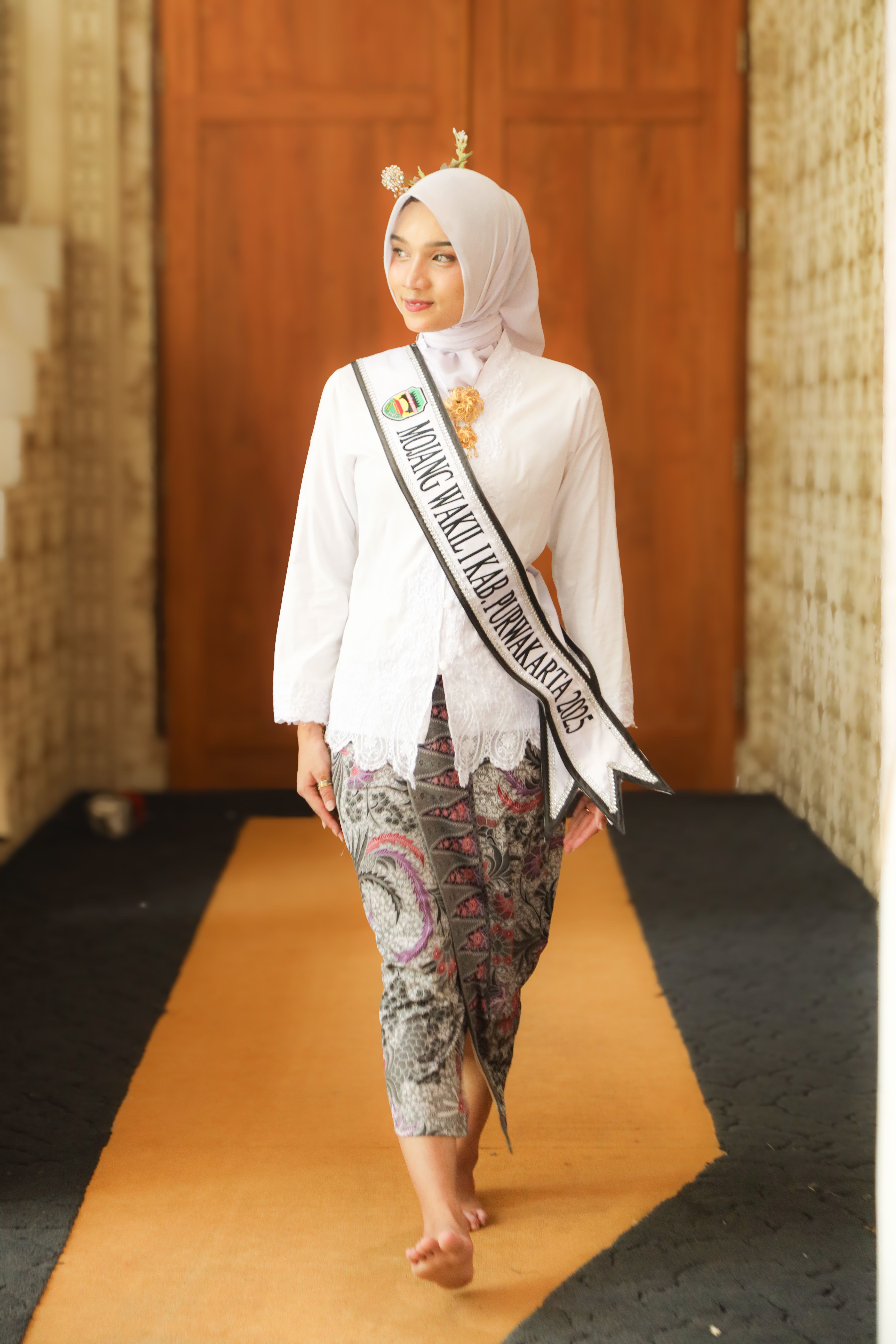 Young woman in traditional Indonesian attire wearing a sash, showcasing cultural fashion.