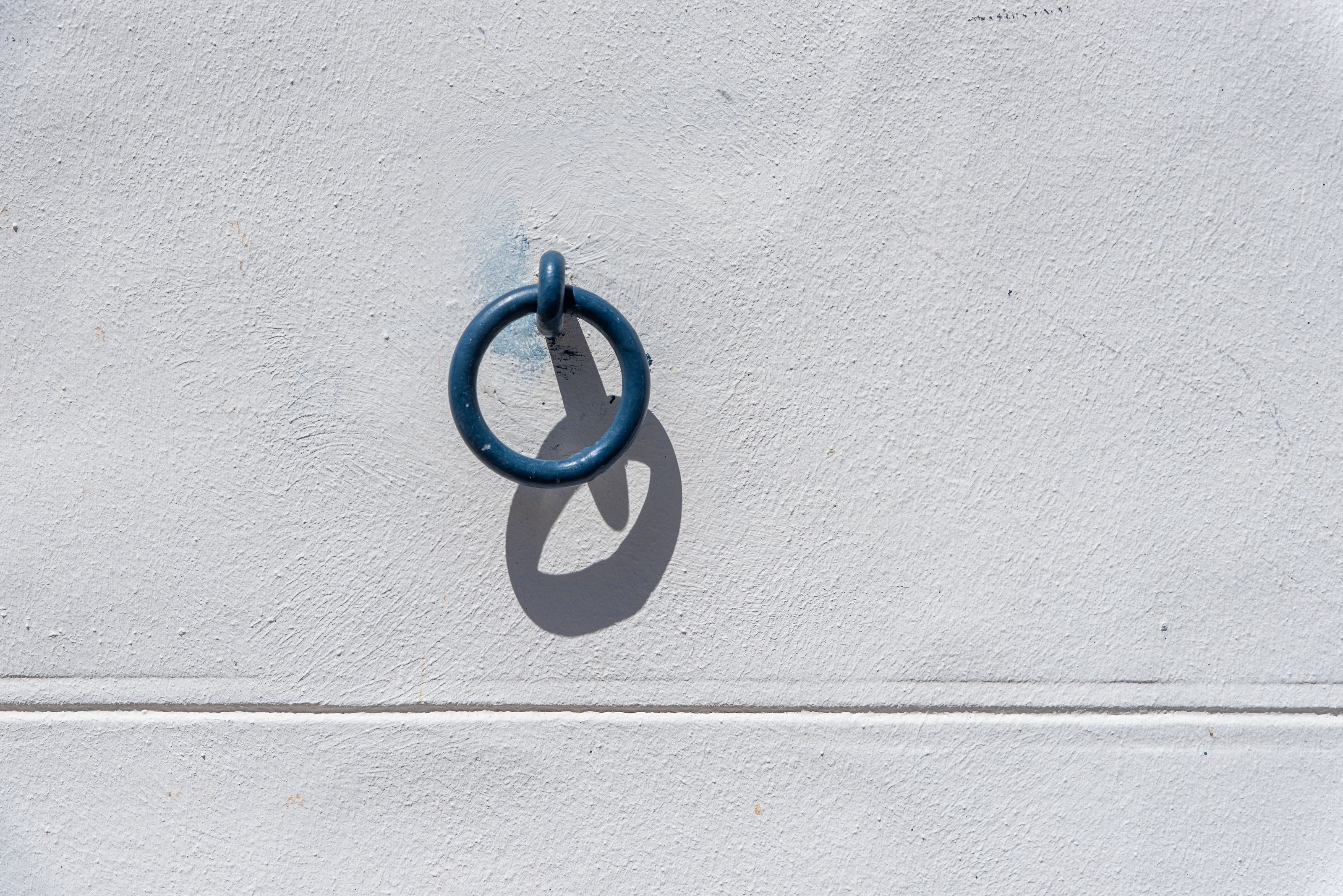 A blue metal ring casts a shadow on a white wall, creating a minimalist visual effect.