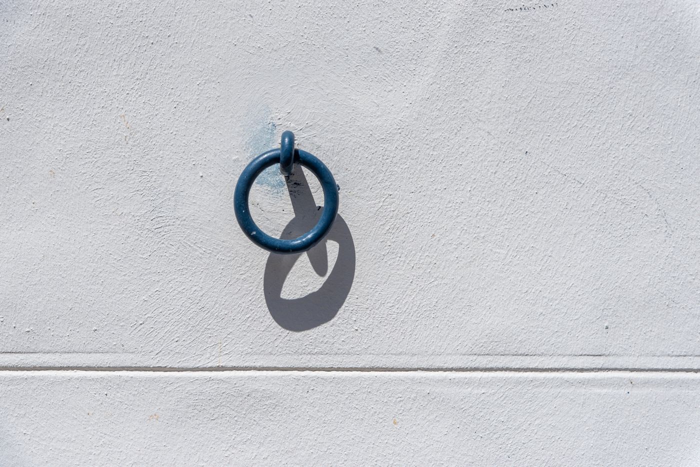 A blue metal ring casts a shadow on a white wall, creating a minimalist visual effect.