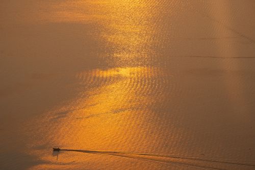 Free A boat sails across shimmering golden waters during sunset on Lake Atitlán, Guatemala. Stock Photo