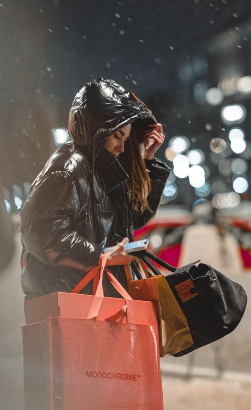 Free Woman in winter attire holds shopping bags in a city at night. Stock Photo
