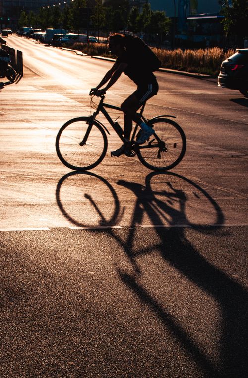 Free A silhouette of a cyclist biking on an urban street during sunset, casting a long shadow. Stock Photo