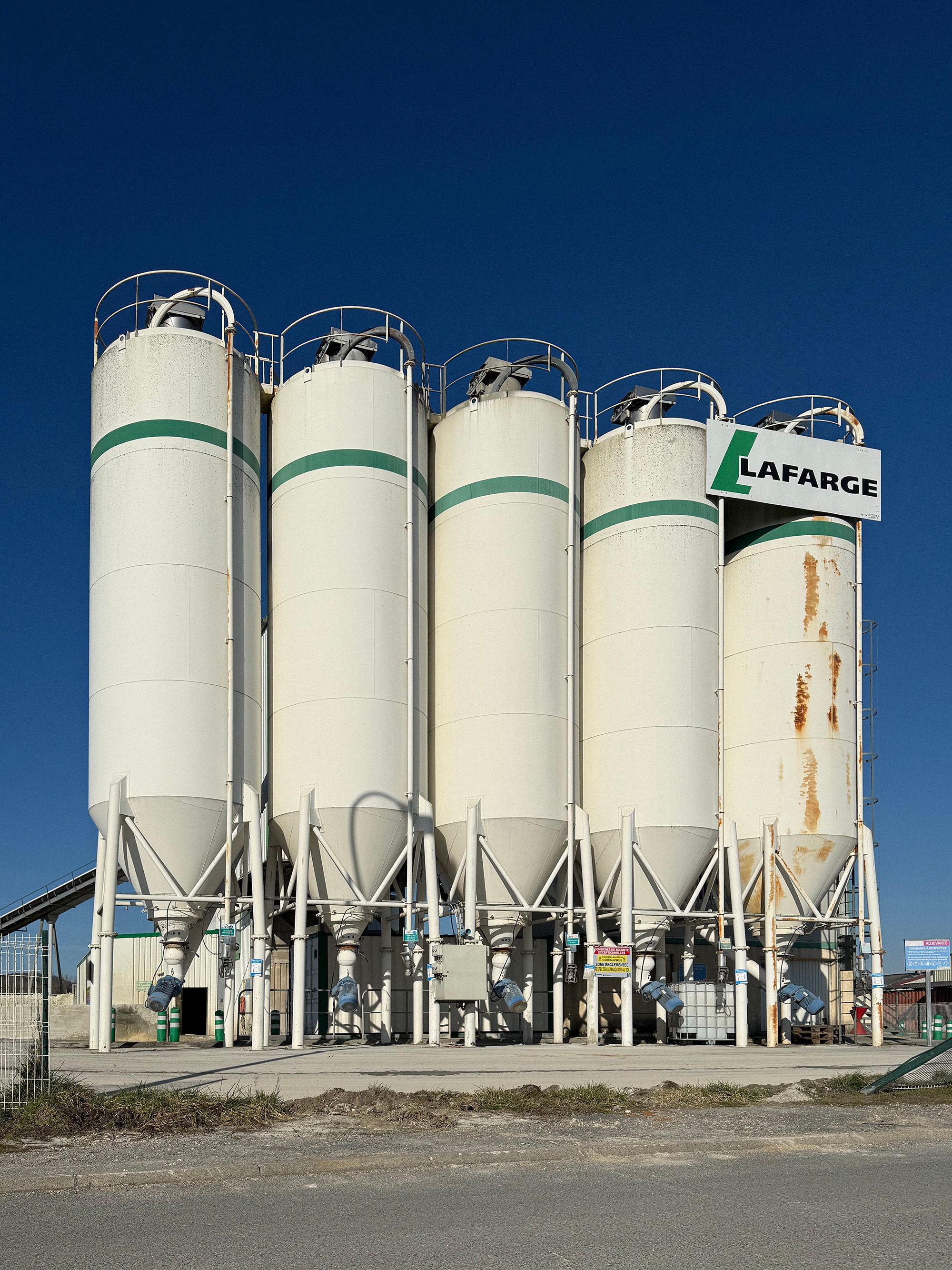 Large white industrial silos at a factory in Boulazac Isle Manoire, France under a bright blue sky.