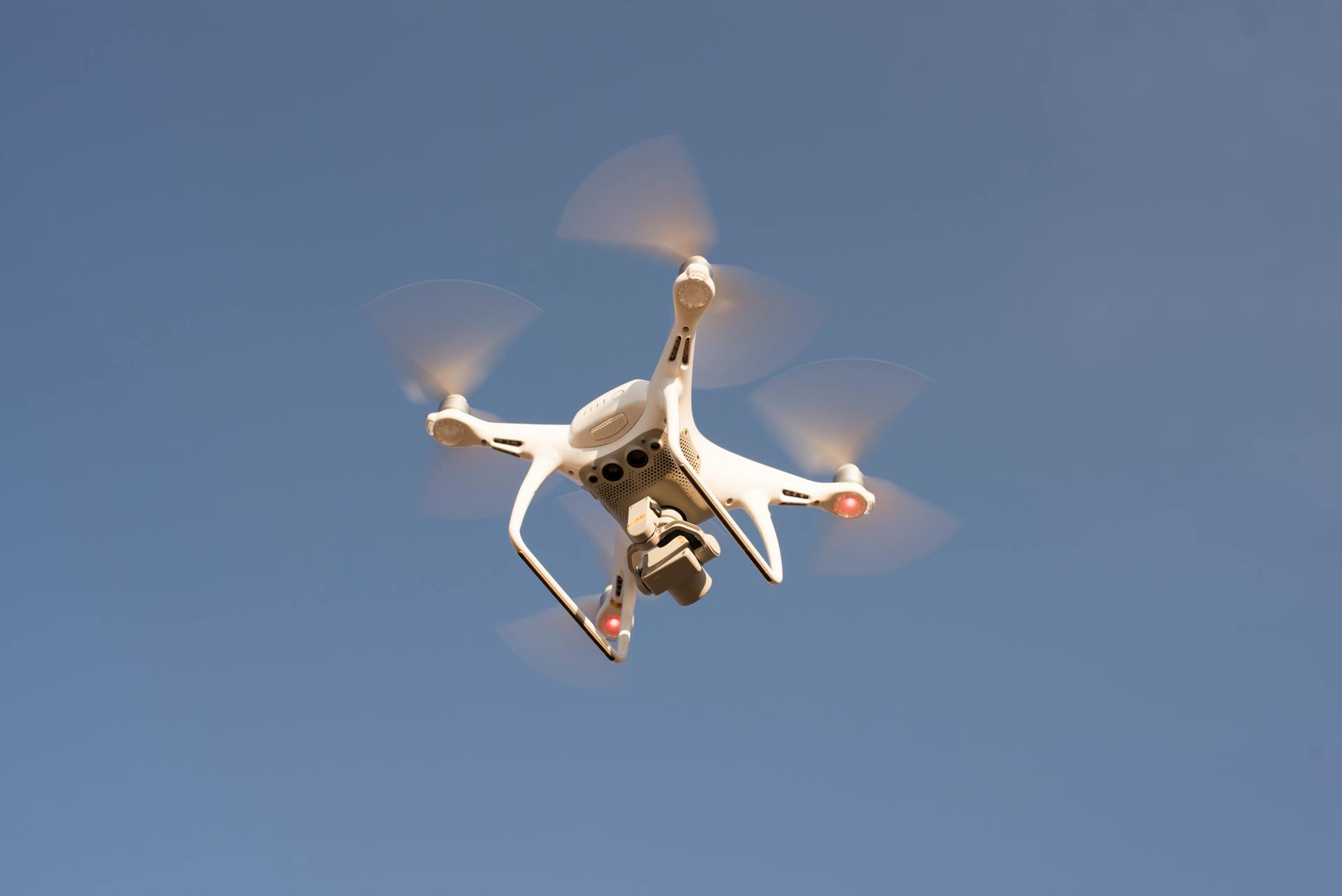 A white drone in flight against a clear blue sky, capturing aerial footage with precision.