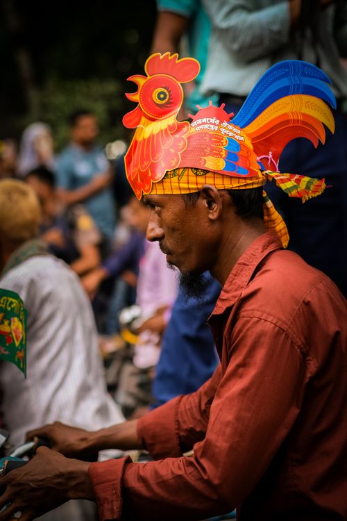 Free Man with a vibrant rooster hat at a lively outdoor gathering, showcasing cultural flair. Stock Photo