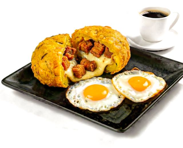 Delicious Ecuadorian breakfast featuring mote pillo, fried eggs, and coffee on a black plate.
