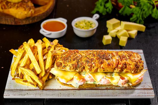Delicious gourmet sandwich with golden fries and dipping sauces on a wooden board.