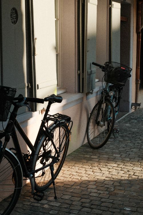 Free Two bicycles parked against a building, casting shadows on cobblestone in Zug, Switzerland. Stock Photo