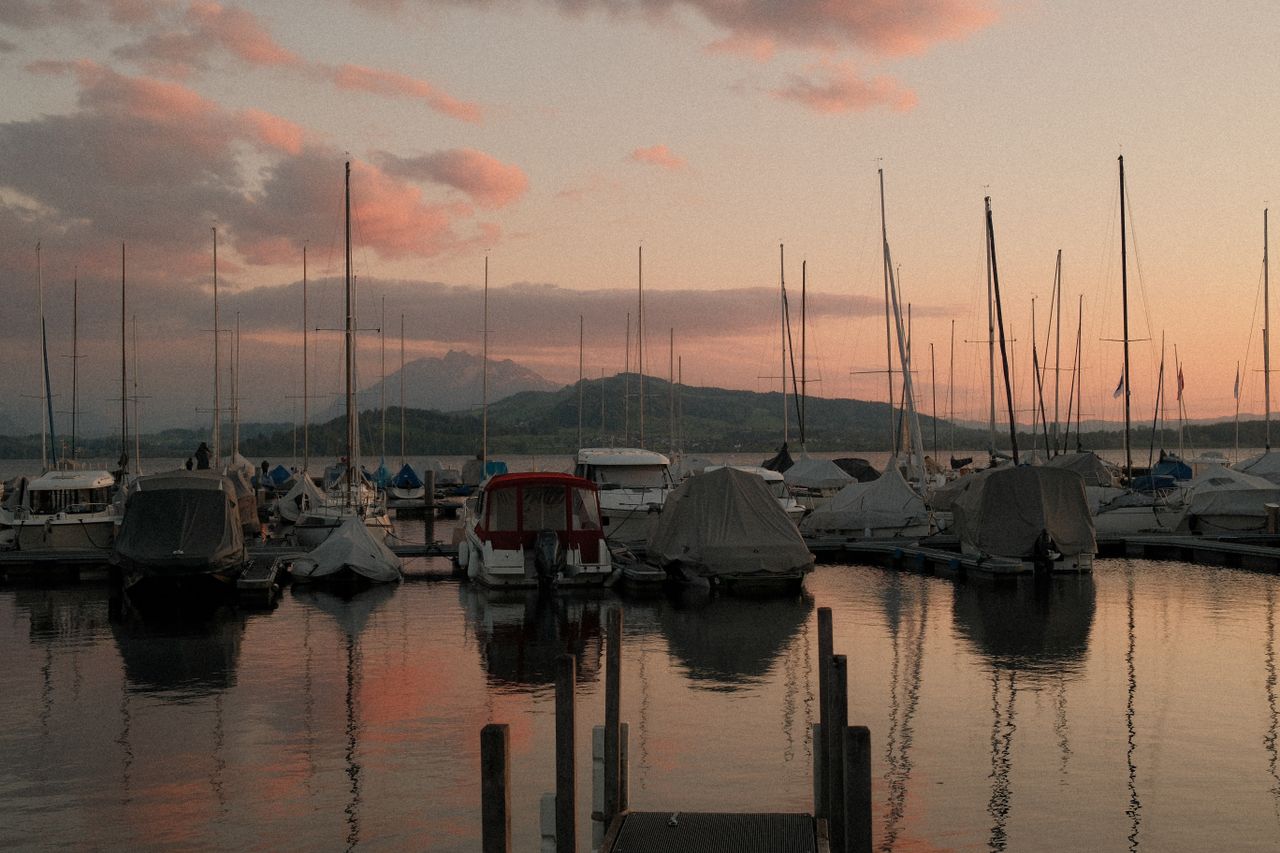 Peaceful scene of boats docked at a marina under a vibrant sunset in Zug, Switzerland.