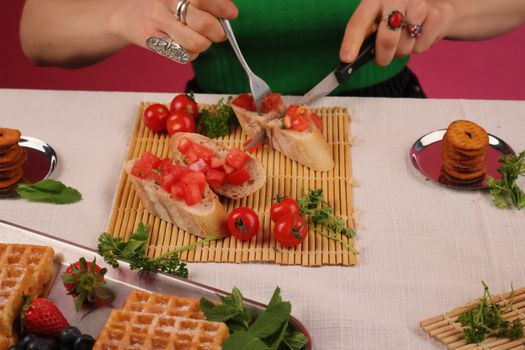Close-up shot of a person preparing bruschetta with fresh vegetables and bread on a dining table.