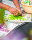 Crop unrecognizable person smashing bright green sprouts with hands before stuffing food while working in garden