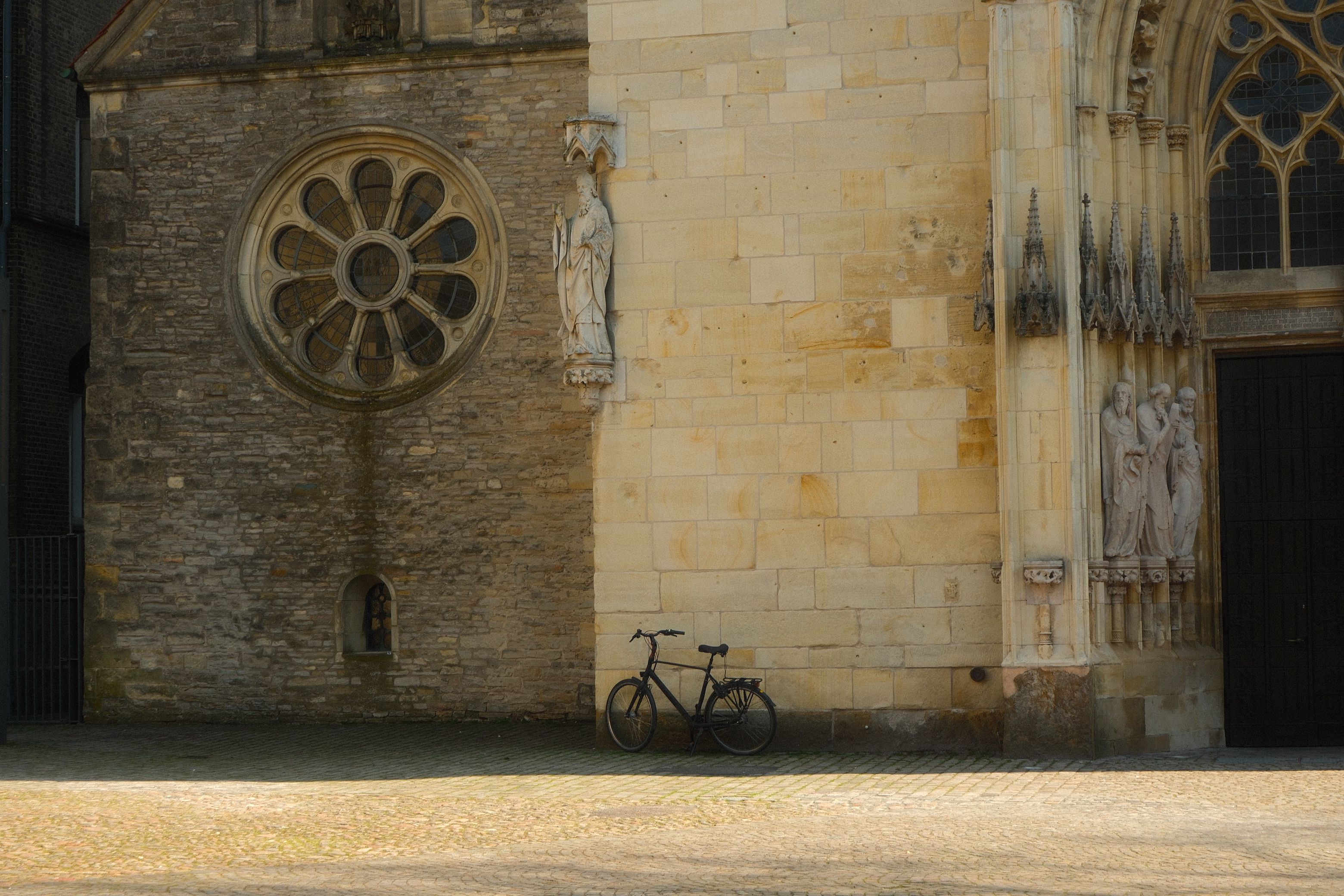 Ein Fahrrad lehnt an der kunstvoll gestalteten Steinmauer einer historischen Kirche in Münster