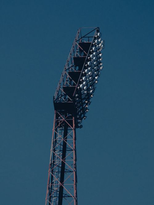 Free A tall stadium floodlight tower stands against a clear blue sky, showcasing its intricate metal structure. Stock Photo
