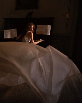 A woman in a flowing dress plays the piano in a dimly lit room, creating a melancholic atmosphere.