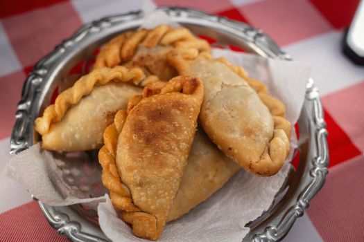 A close-up view of freshly cooked Argentine empanadas served on a vintage plate with a checkered tablecloth.
