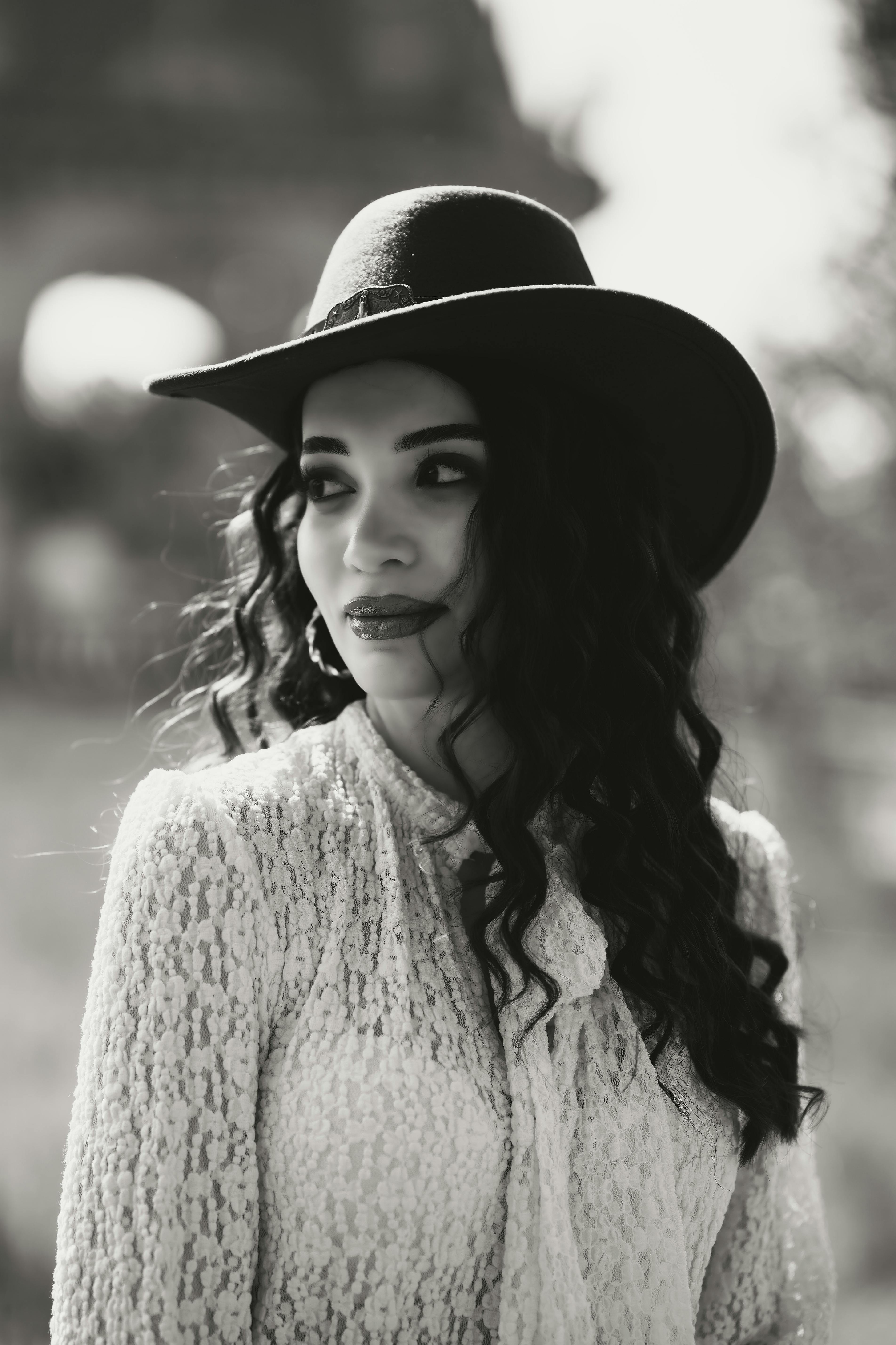 Black and white portrait of an elegant woman in a lace blouse and black hat with soft curls.