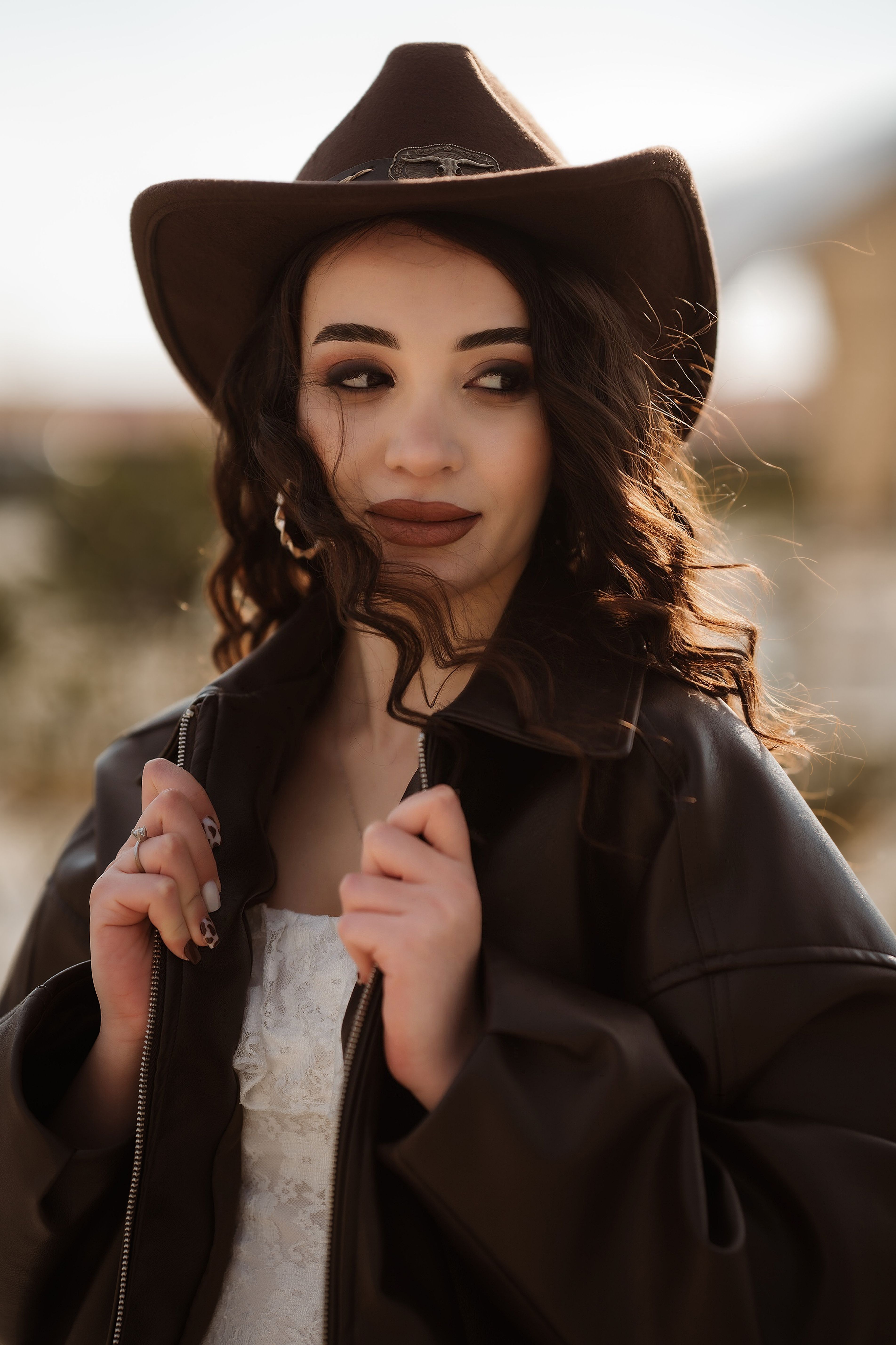 Portrait of a fashionable woman wearing a cowboy hat and leather jacket in a sunny outdoor setting.