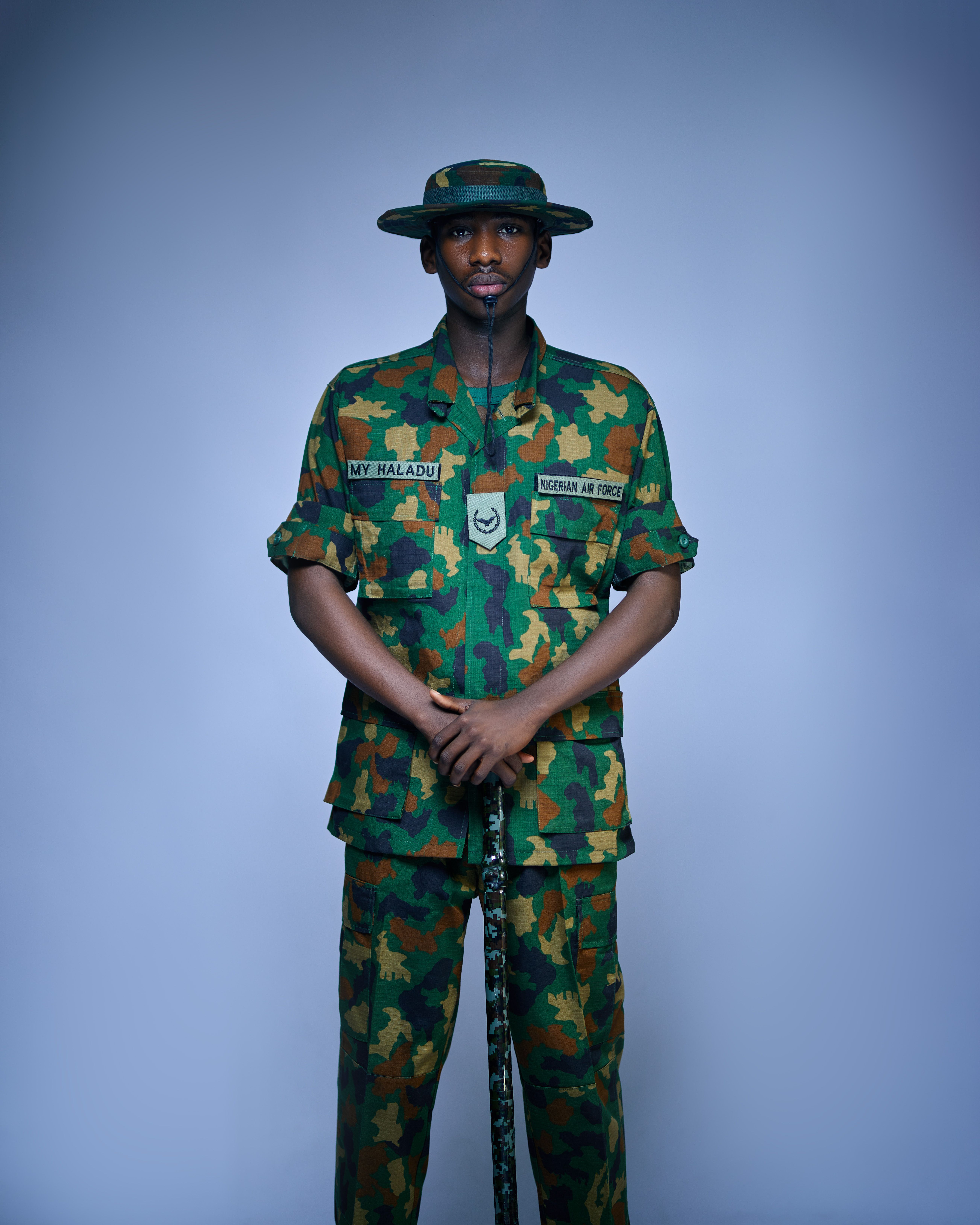 Camouflage-clad soldier stands at attention in studio setting.