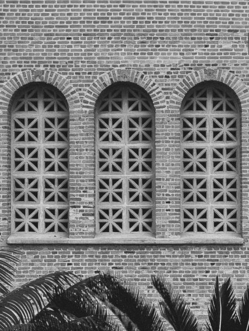 Three arched brick windows with lattice designs on a brick facade in Aparecida, Brazil.