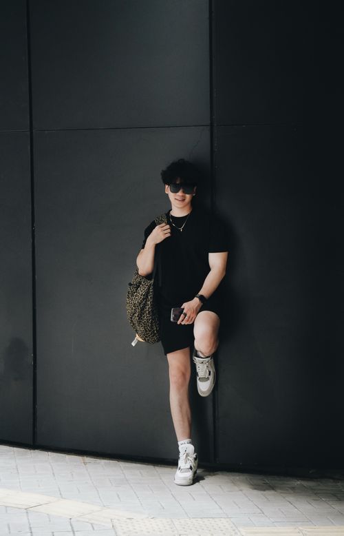 Free Trendy young man in black attire leaning against a wall with cool demeanor. Stock Photo