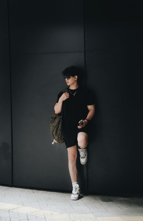 Free Young adult in trendy streetwear leaning on a dark urban wall, showcasing modern style. Stock Photo