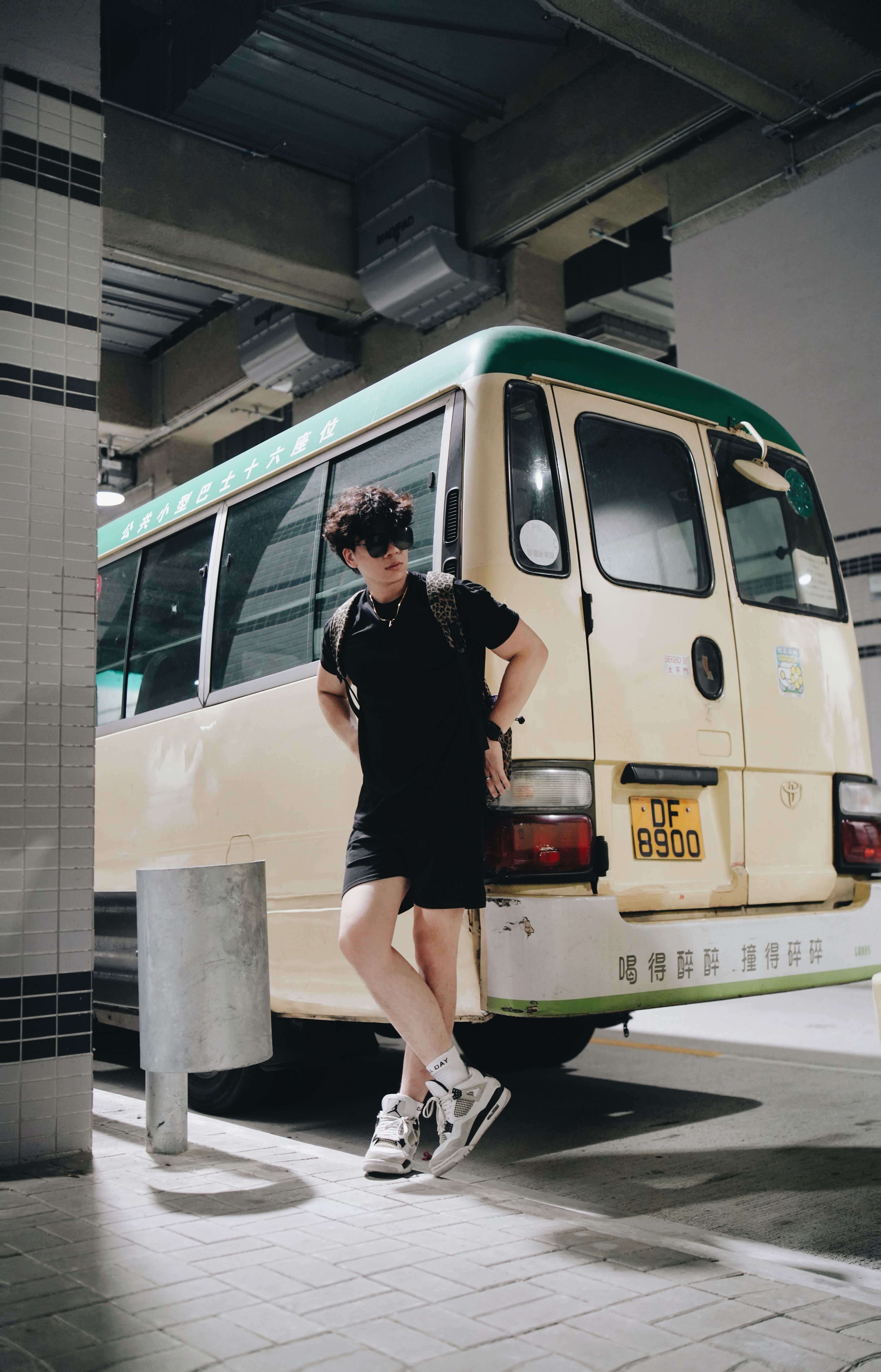 Stylish young man in urban outfit leaning on a vintage minibus parked in an underground garage.