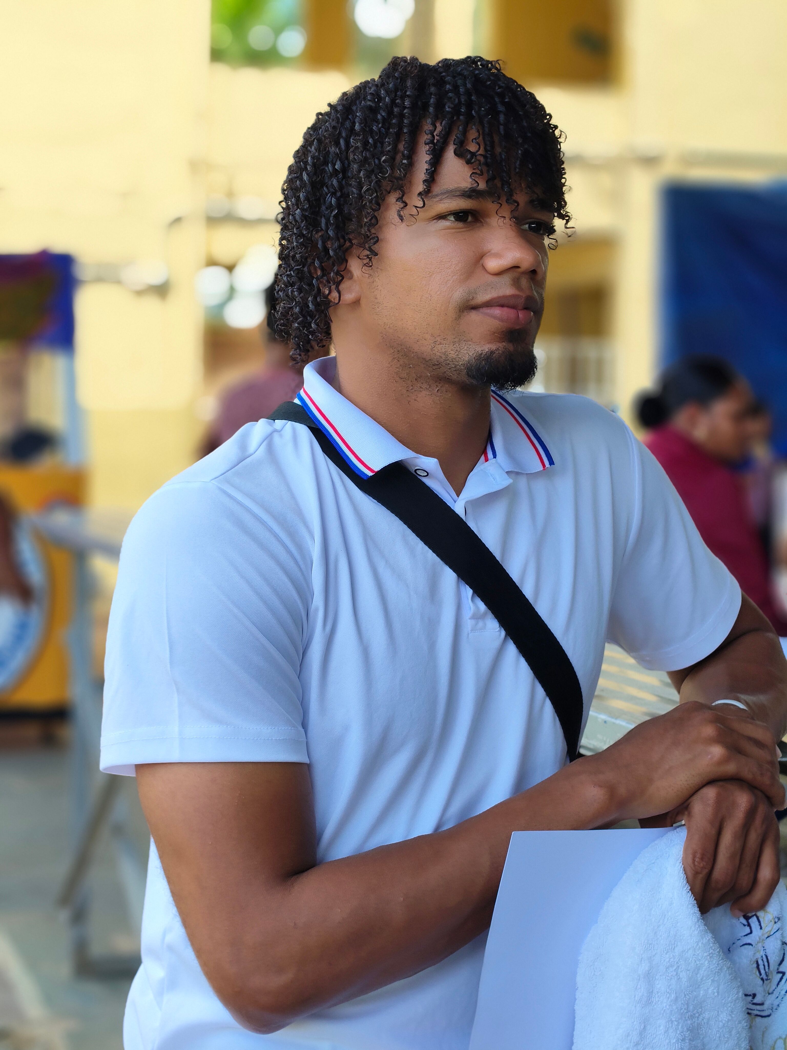 Casual portrait of a young man with curly hair outdoors on a sunny day.