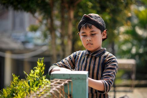 Free Young Indonesian boy wearing traditional clothing in an outdoor setting, focused on an activity. Stock Photo