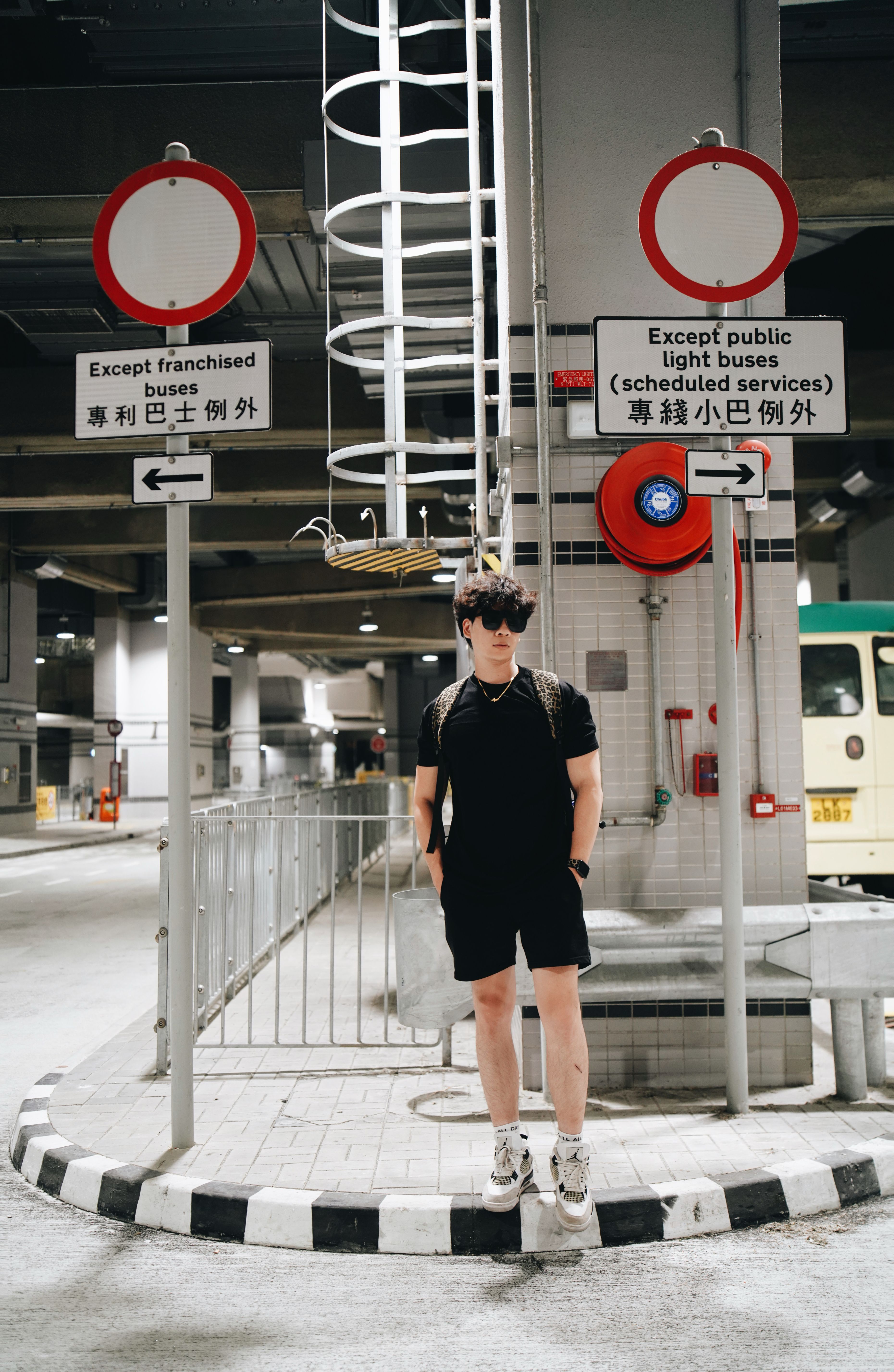 Man in black outfit under urban signage in modern transit area.