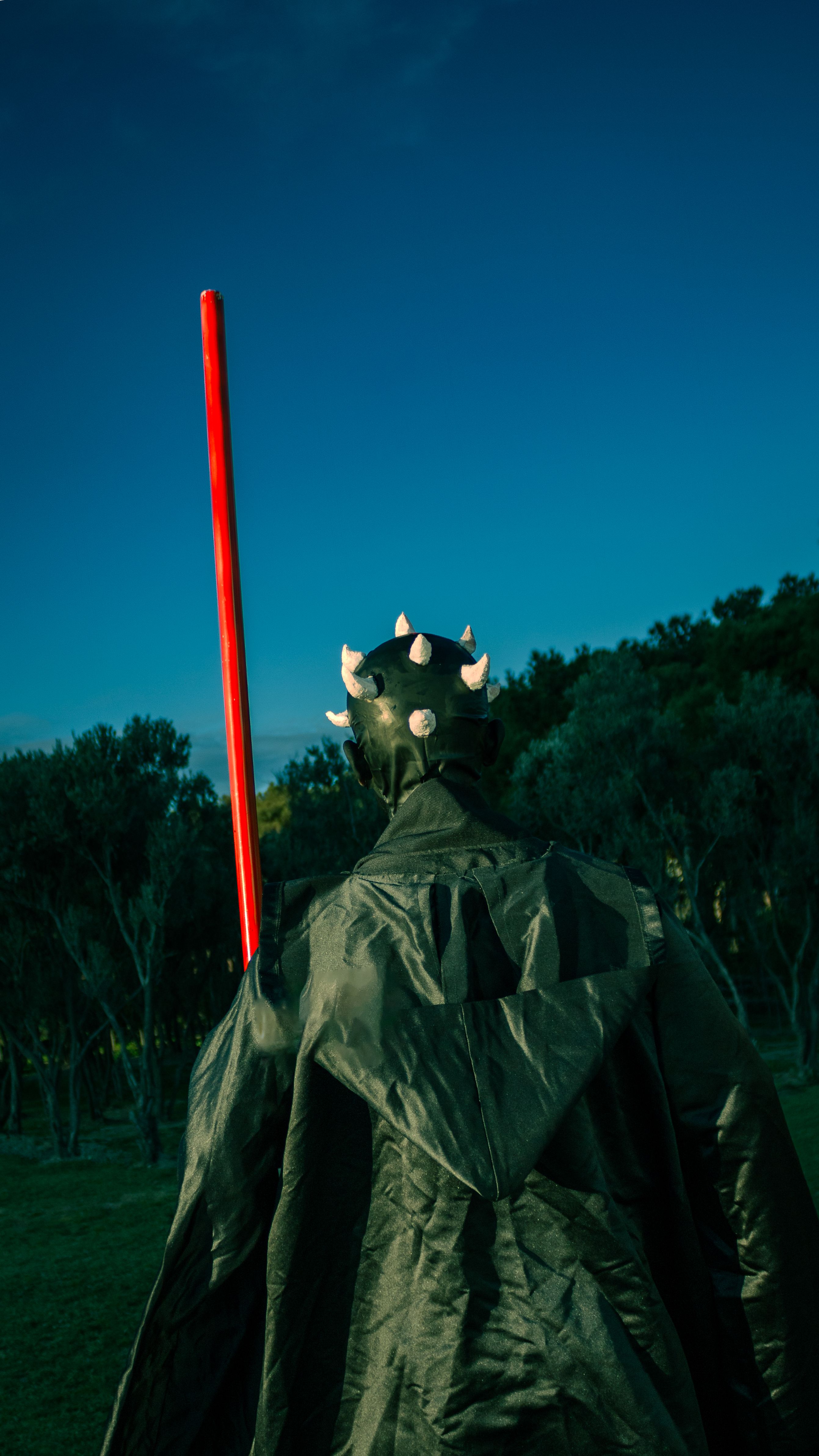 A dramatic cosplay scene with a figure holding a red lightsaber in a park-like setting in Baku, Azerbaijan.