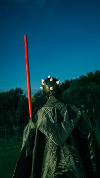 A dramatic cosplay scene with a figure holding a red lightsaber in a park-like setting in Baku, Azerbaijan.