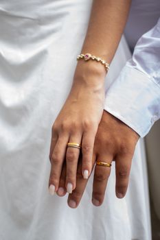 A couple's hands intertwined, showcasing gold wedding bands in an intimate setting.