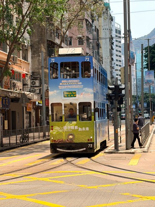 Free A blue tram navigates a sunny street in bustling Hong Kong, showcasing urban life. Stock Photo