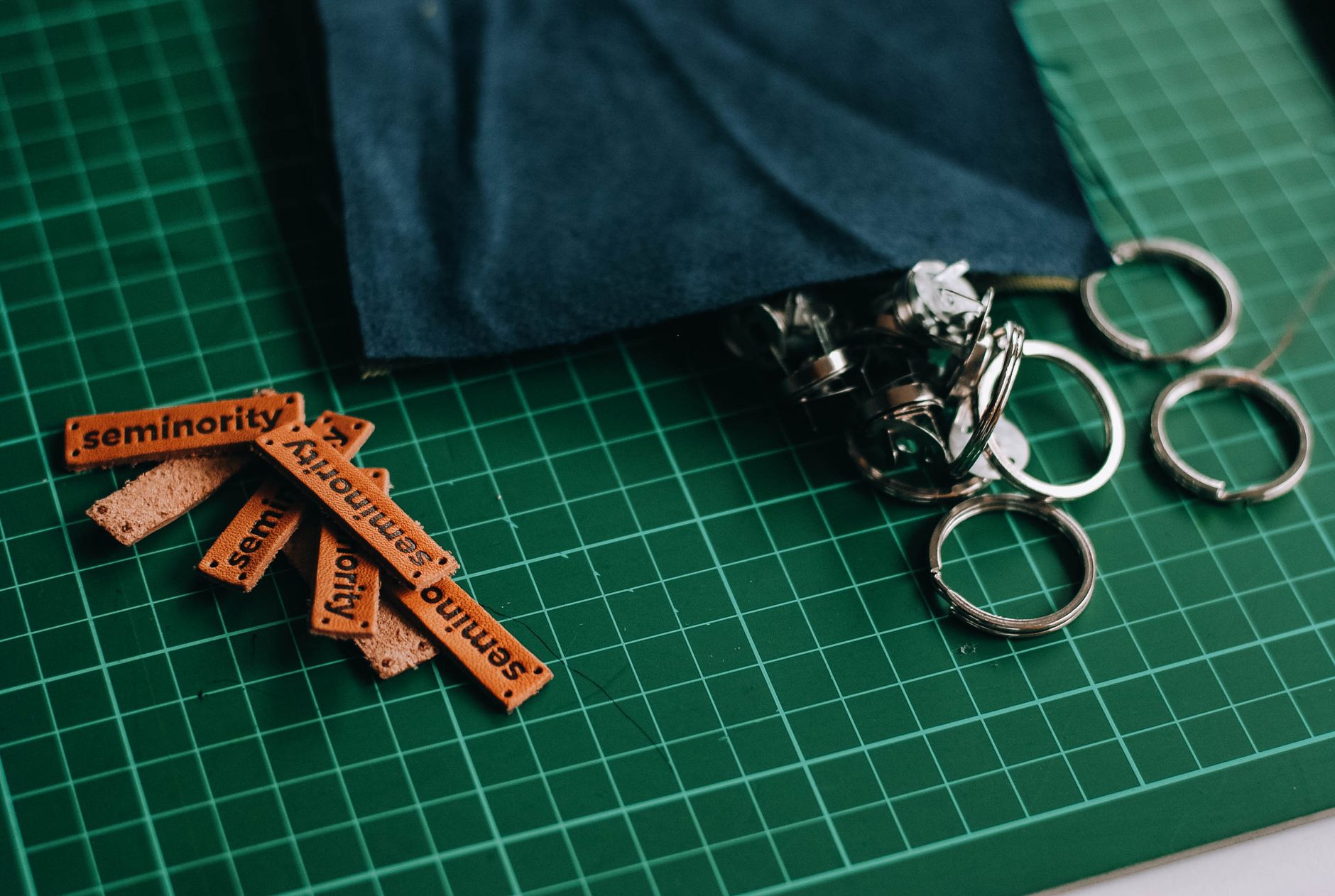 Close-up of leather tags labeled 'seminority' and metal rings on a green cutting mat, ideal for crafting themes.