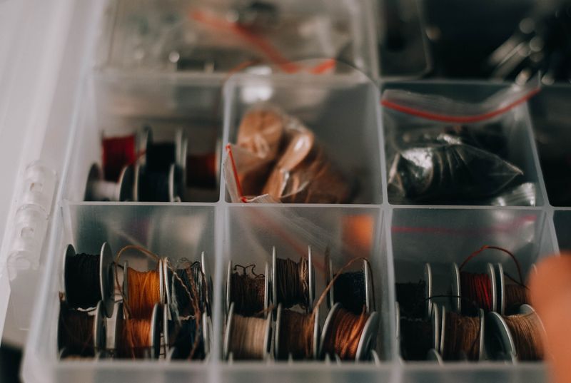 Assorted colorful sewing threads neatly arranged in a clear organizer box on a craft table