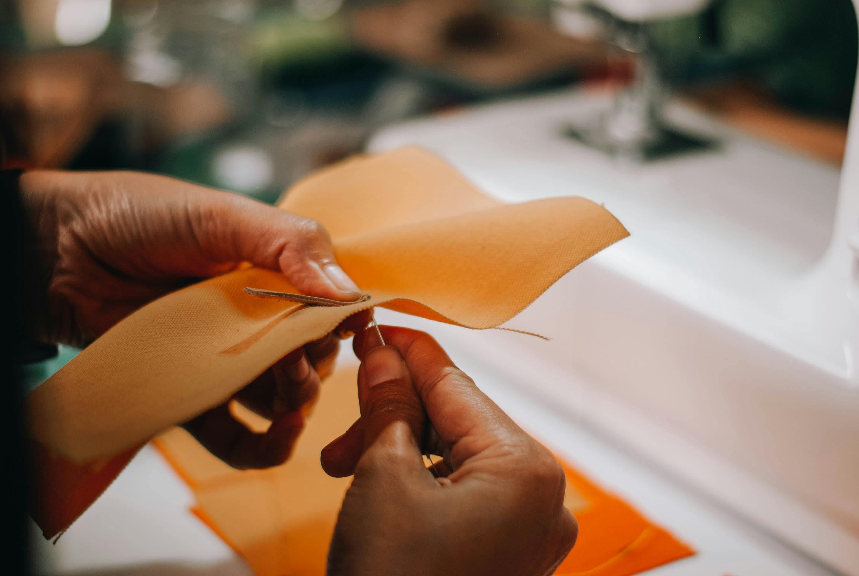 Detailed view of hands sewing orange fabric with needle and thread. Ideal for DIY and crafting projects. — Maynard Longarm Quilting