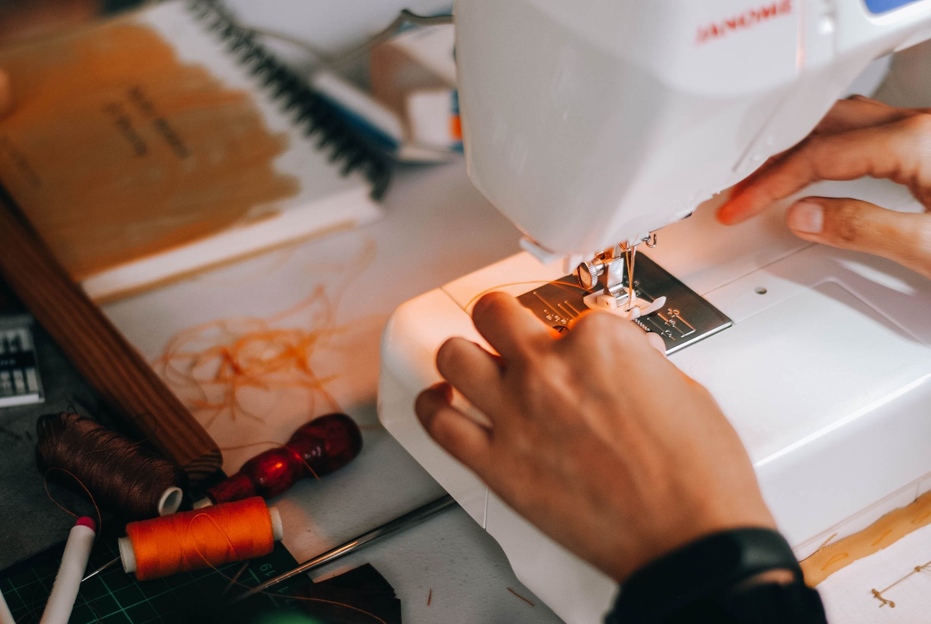 A person sewing with a machine, surrounded by sewing tools and thread.