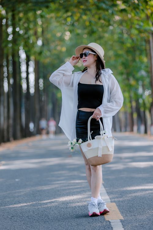 Free Fashionable woman in sunglasses and hat walking down a tree-lined path outdoors. Stock Photo