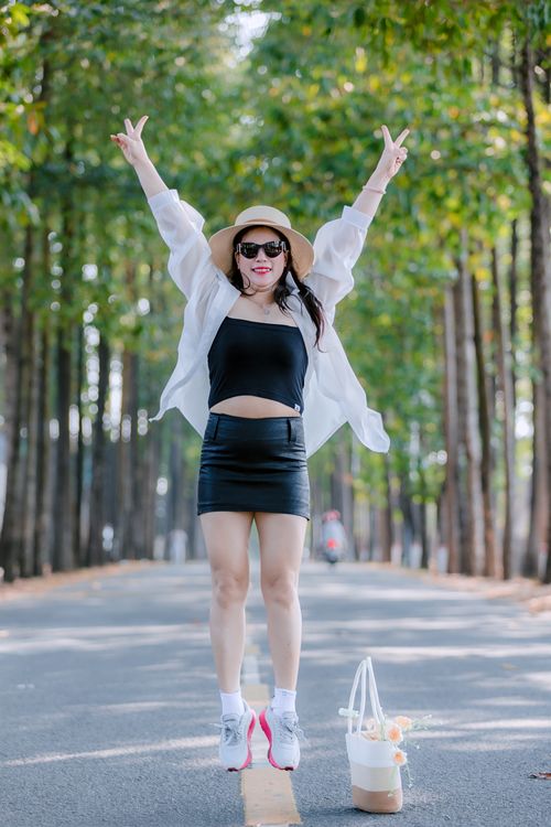Free Stylish woman in summer attire joyfully jumps on a forested road. Stock Photo