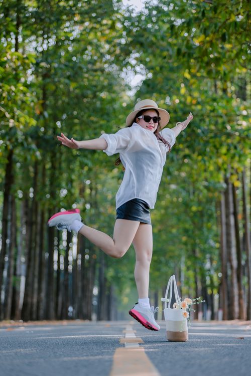 Free Happy woman in casual outfit jumps joyfully on beautiful tree-lined road. Stock Photo