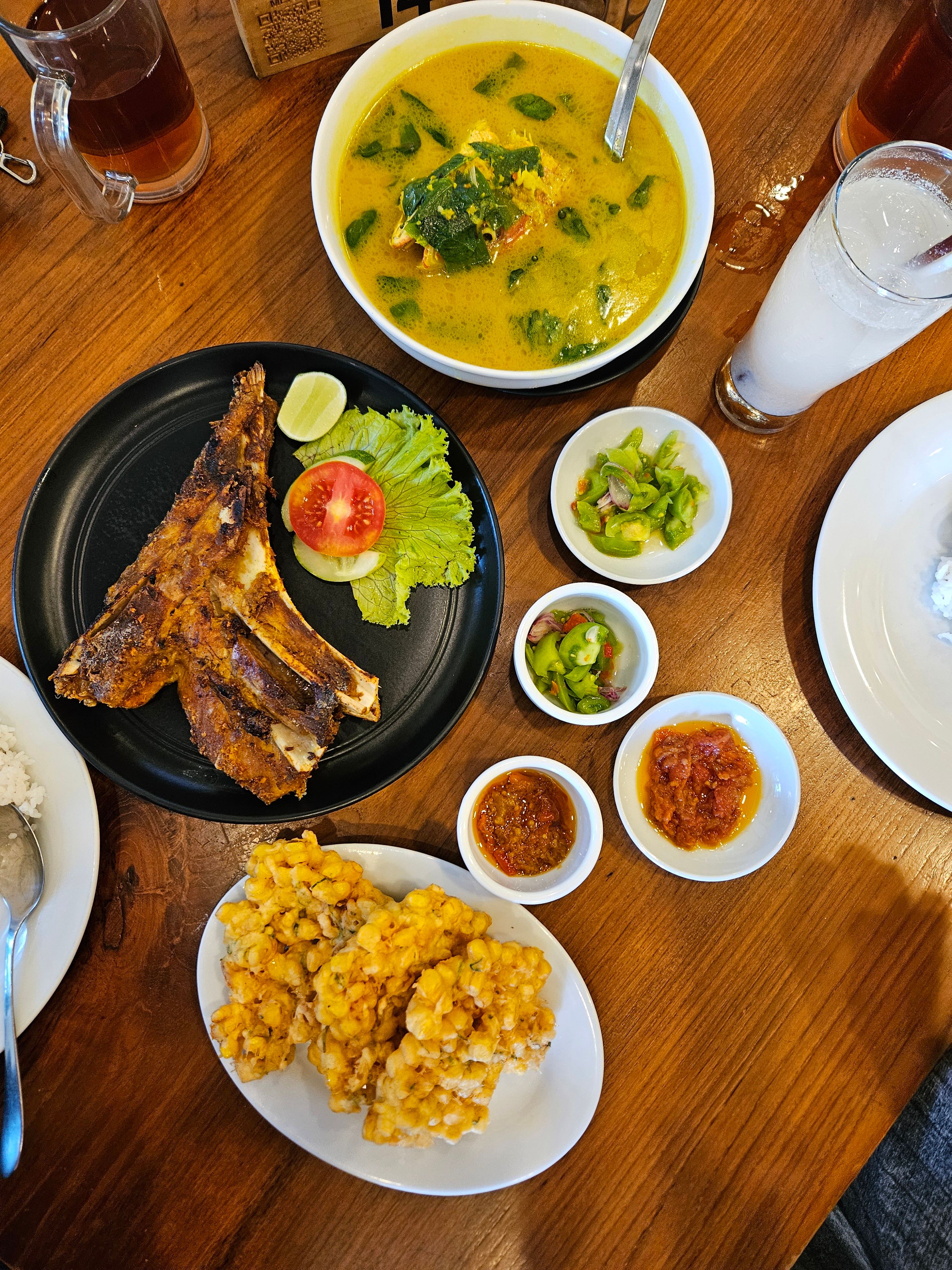Indonesian meal featuring grilled ribs, corn fritters, and vegetable soup, vibrant and appetizing.