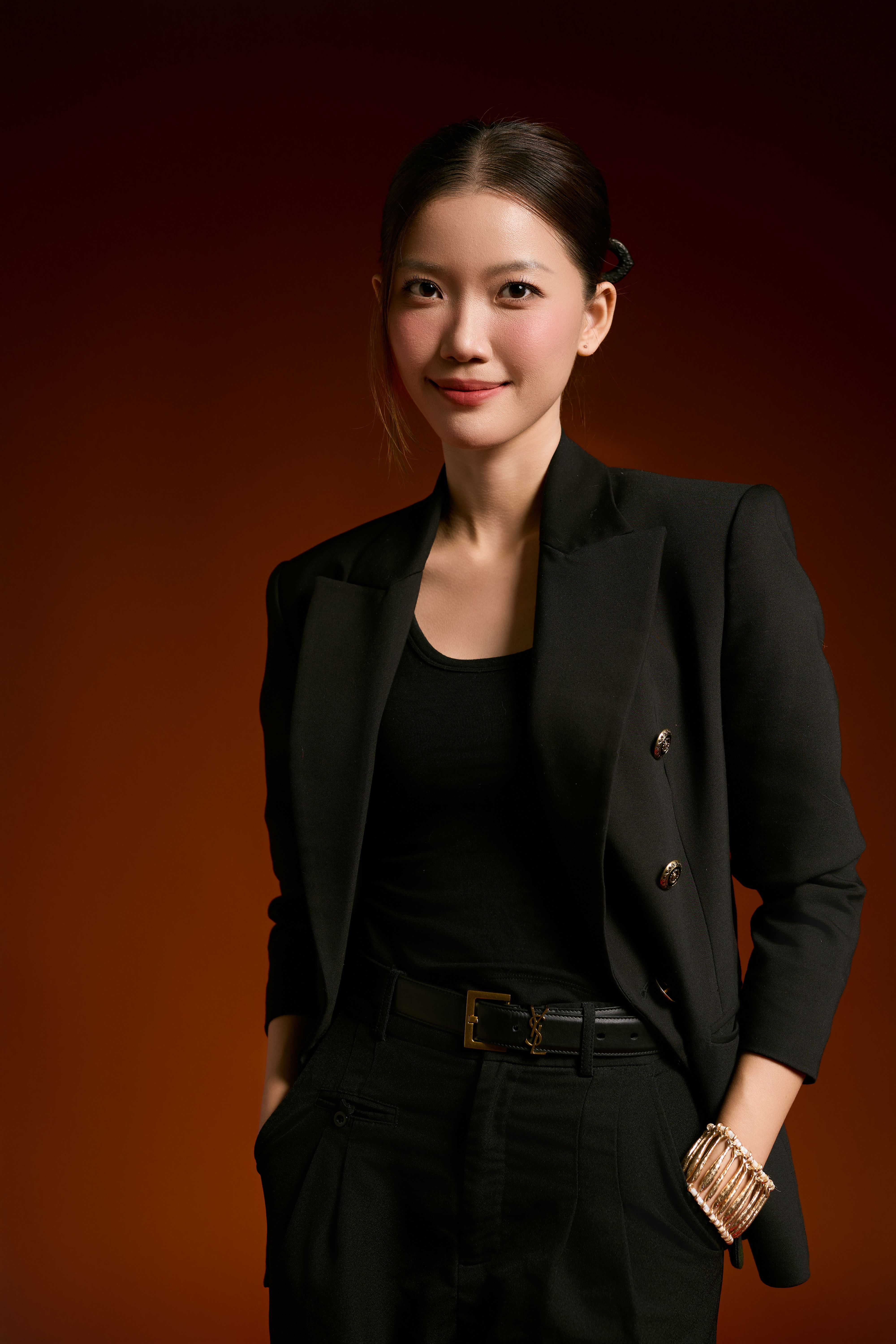 Confident woman in a black blazer standing against a warm brown background.