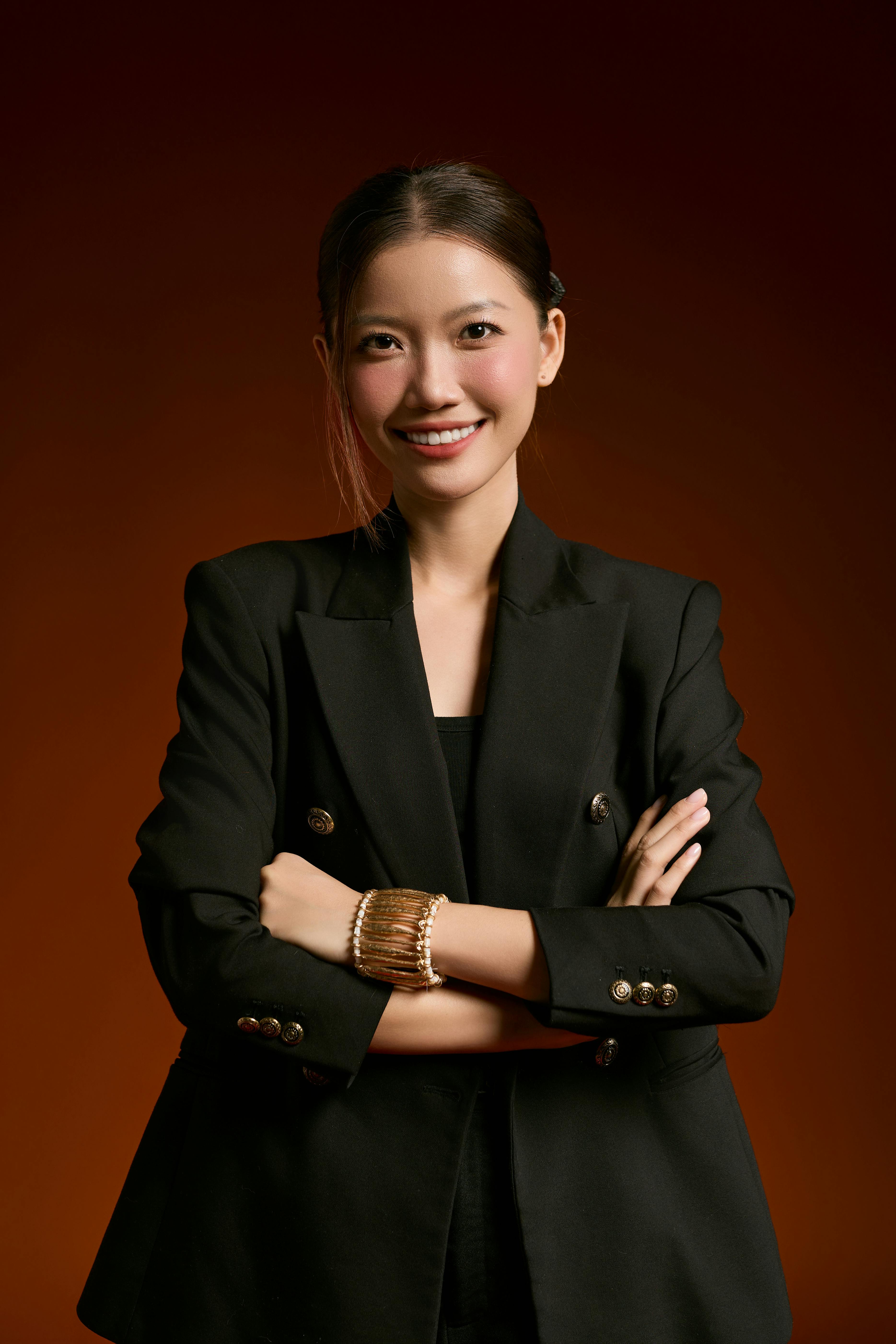 Portrait of a confident smiling businesswoman in a black suit against a brown background, exuding professionalism.