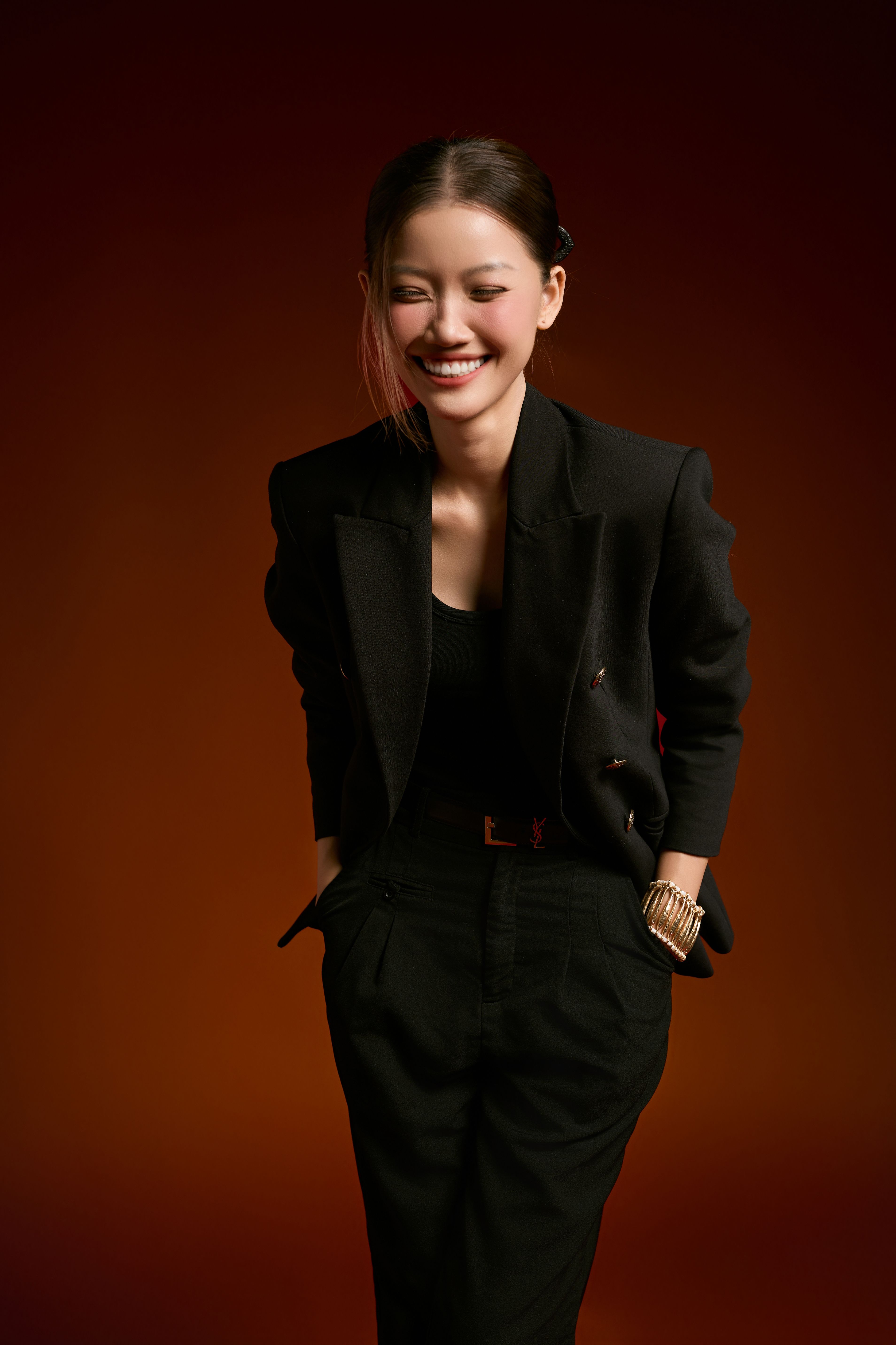 Elegant studio portrait of a smiling woman in a black suit against a warm background.